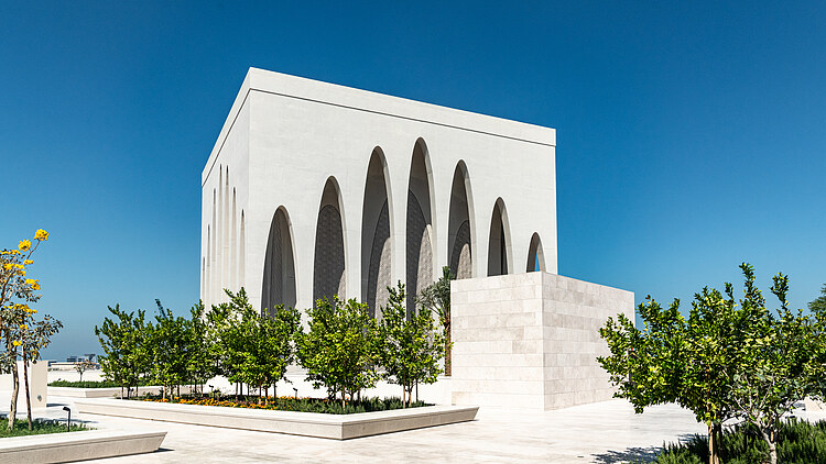 Modern building of the Abrahamic Family House on Saadiyat Island, featuring distinctive white architecture, tail arches and a landscaped forecourt under a clear blue sky