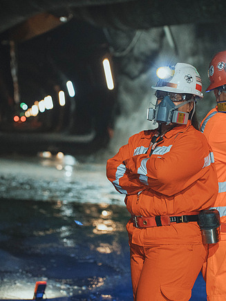 Beleuchtete Bergbauarbeiten in einer Höhle mit zwei Arbeitern, die eine Maske tragen