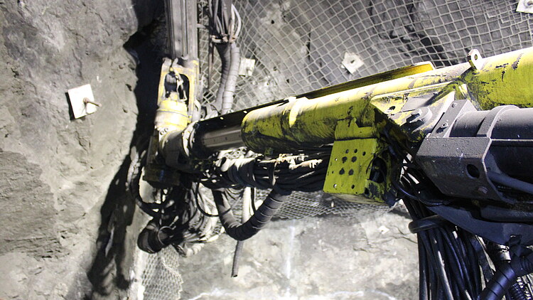 Hydraulisches Bohrgerät im Einsatz in einem unterirdischen Stollen. Sichtbar sind die Ortsbrust, technische Infrastruktur und die für den Untertagebau erforderlichen Versorgungseinrichtungen.