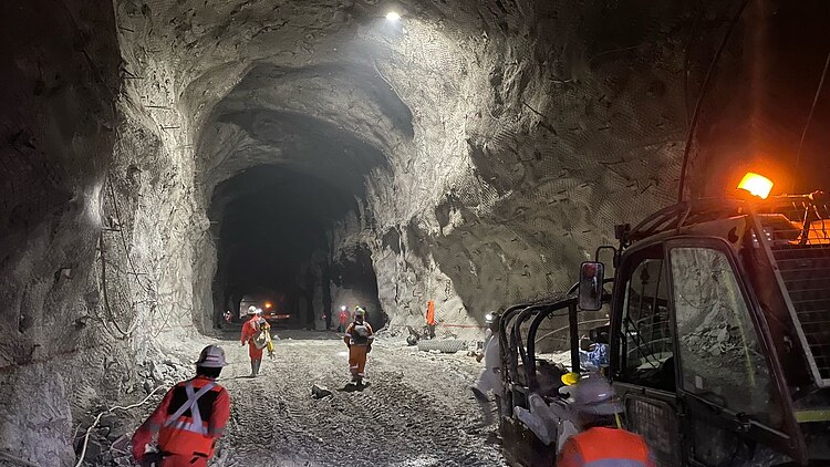 Unterirdischer Stollen der Mine El Teniente in Chile mit Mitarbeitenden in Schutzausrüstung, Arbeitsfahrzeugen, ausgebauten Felswänden und technischer Infrastruktur.