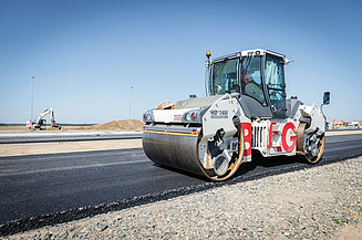 Road roller compacting a newly laid asphalt surface during road construction works.