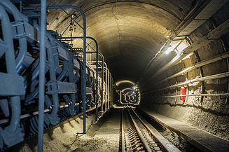 Interior view of a railway tunnel with tracks, cable systems and technical installations forming part of the tunnel infrastructure.