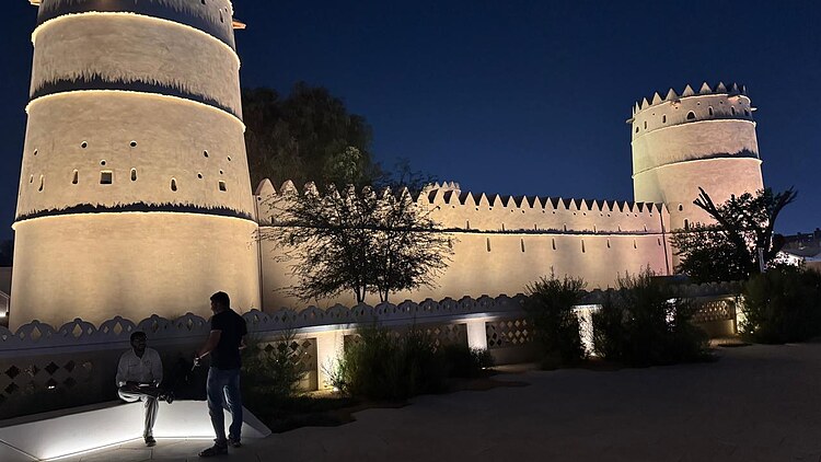 Illuminated Al Ain Museum in Abu Dhabi featuring traditional towers, defensive walls and landscaped outdoor areas at night.