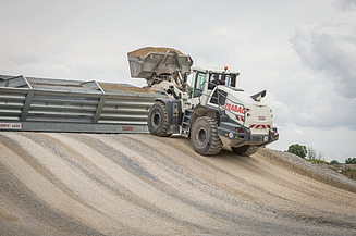 Radlader bei Erdbewegungs- und Dammbauarbeiten auf einer Großbaustelle mit aufgeschütteten Erdmassen und Baustelleninfrastruktur.